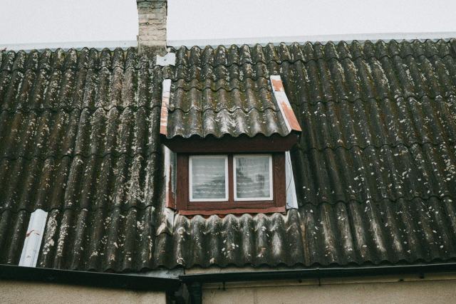 Le diagnostic amiante d'un logement vendu, de la visite aux suites du rapport Toiture en plaques ondulées de type fibrociment couvertes de mousse, lucarne au centre