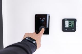 Doigt qui appuie sur un thermostat d'ambiance numérique fixé au mur