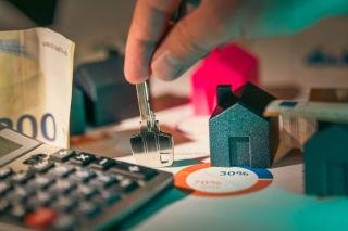 Petites maisons en bois, clé, calculatrice et billets réunis sur un bureau