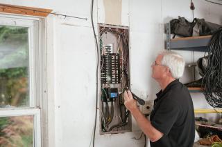 Homme aux cheveux blancs qui contrôle un tableau électrique ouvert au mur d'une maison