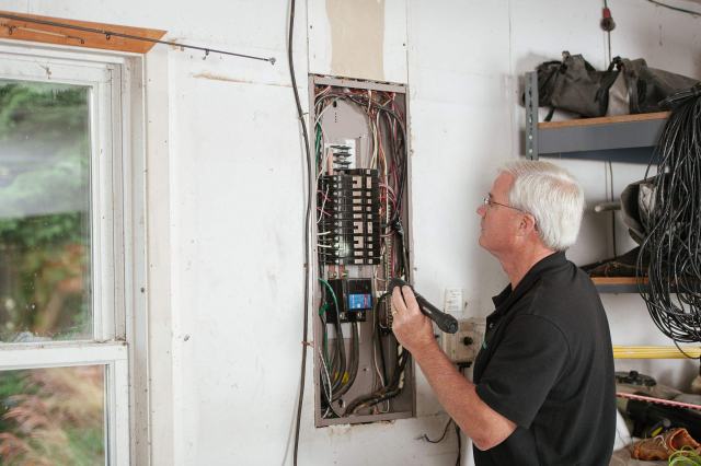 État de l'installation électrique : contrôle, anomalies et validité Homme aux cheveux blancs qui contrôle un tableau électrique ouvert au mur d'une maison