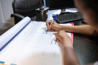 Main qui note des échéances sur un grand calendrier mensuel posé sur un bureau