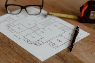 Plan d'appartement imprimé avec mètre ruban, stylo et lunettes sur un parquet