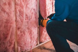 Artisan ganté qui pose des rouleaux de laine minérale entre les montants d'un mur