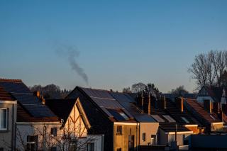 Toits de maisons mitoyennes équipés de panneaux solaires au crépuscule, fumée de chauffage dans le ciel froid