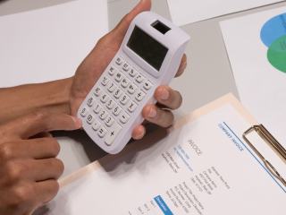 Mains tenant une calculatrice au-dessus d'un devis chiffré et de graphiques