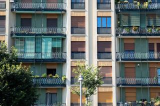 Façade d'immeuble en copropriété aux balcons vitrés et touches de vert, arbres devant l'entrée