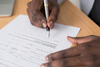Mains qui signent un document au stylo plume sur une table en bois