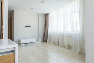 Séjour d'appartement vide et clair, voilages blancs et parquet, prêt à être loué