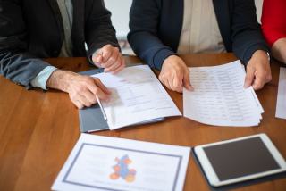Mains qui comparent des devis et tableaux de prix étalés sur une table